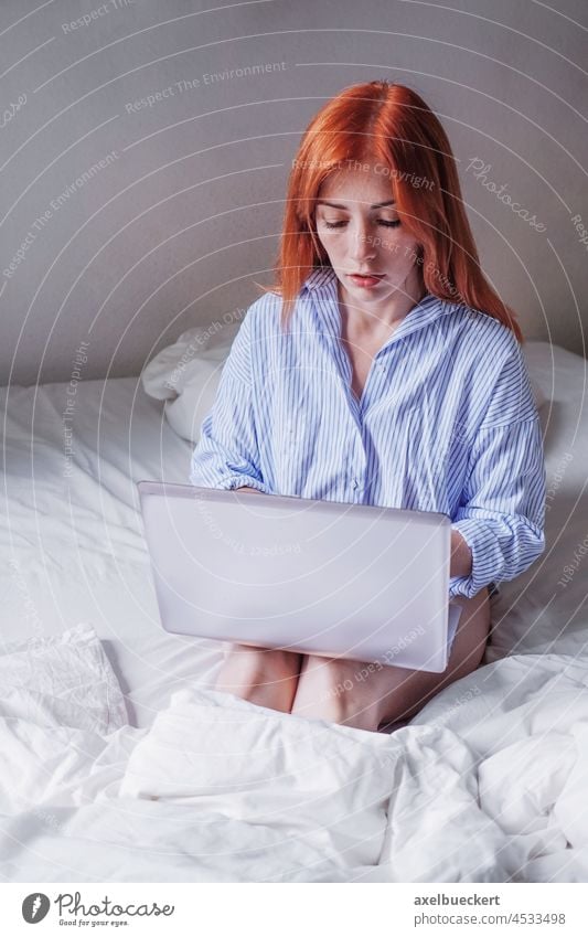 junge Frau im Bett sitzend mit Laptop auf den Knien, die von zu Hause aus arbeitet Computer Homeoffice Arbeit Pyjama benutzend Notebook Schlafzimmer