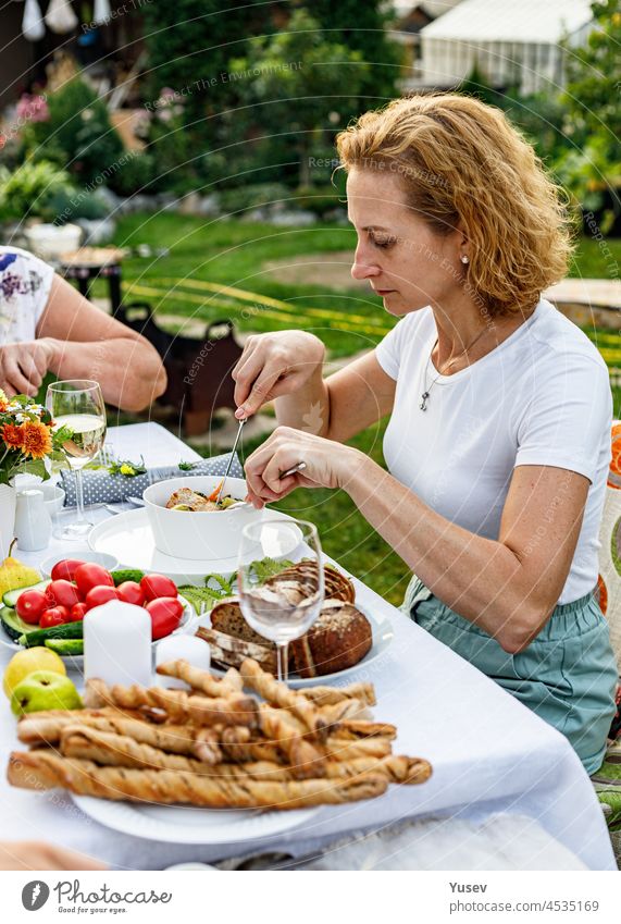 Glückliche Familie bei einem festlichen Abendessen oder Grillfest im Sommergarten. Junge schöne Frau essen köstliche Grill Fleisch und Gemüse. Familie Abendessen in den Hinterhof Konzept. Lebensstil