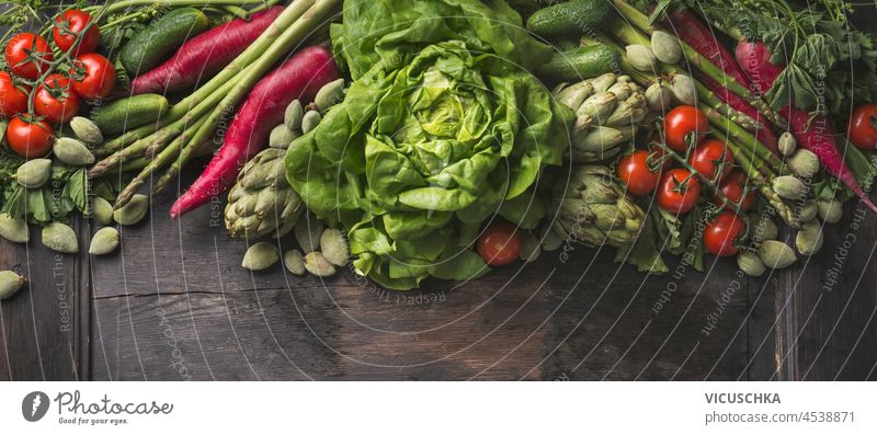 Verschiedene grüne und rote Gemüse auf hölzernen Küchentisch: Salat, Tomaten, Radieschen, Artischocken, Spargel und Gurken. Gesunde plastikfreie Produkte auf rustikalem Hintergrund. Ansicht von oben.