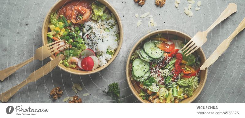 Japans Poke Bowl mit Meeresfrüchten und Salat und vegane Schale mit Gemüse und Kichererbsen in nachhaltigen Lebensmittelbehälter auf grauem Hintergrund. Umweltfreundliche Lieferung von Lebensmitteln mit plastikfreiem Besteck. Ansicht von oben.
