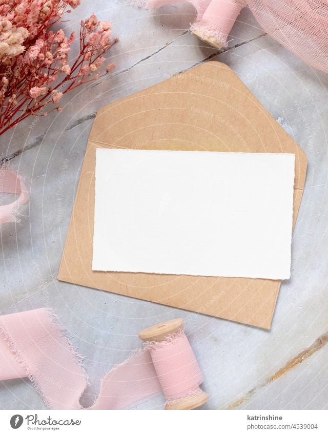 Karte mit Umschlag auf Tisch mit rosa Blumen und Bändern Postkarte Papier blanko Attrappe Hochzeit Kuvert Seide Draufsicht romantisch hellrosa Pastell Heirat