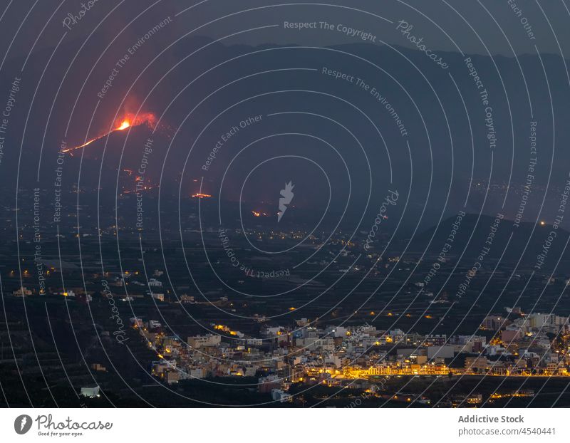 Kleine Siedlung in einem Gebirgstal mit einem ausbrechenden Vulkan Berge u. Gebirge Wohnsiedlung Haus Ambitus Nacht Landschaft Lava Hochland Stadt reisen