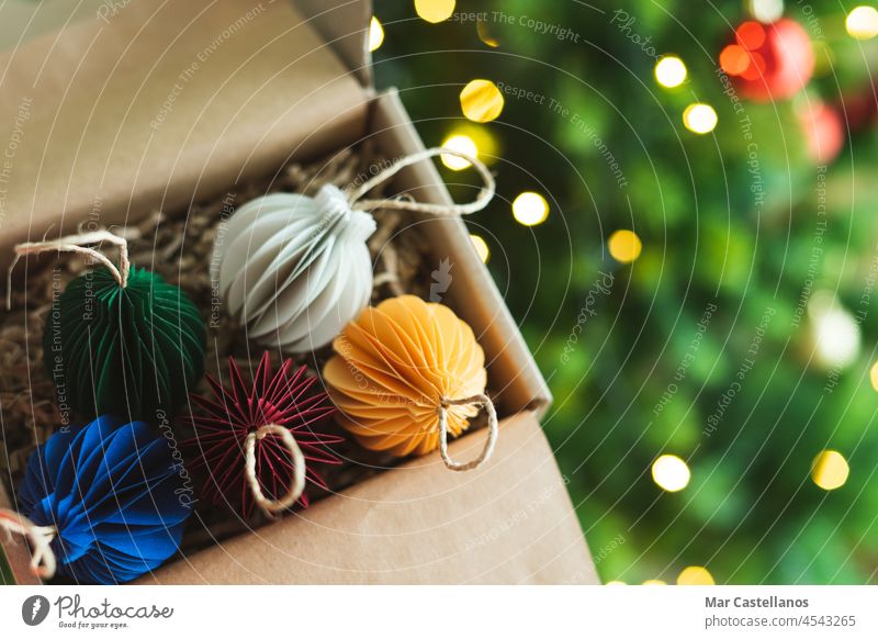 Weihnachtskugeln in einer Schachtel mit Baum und Lichtern im Hintergrund. Platz zum Kopieren. Weihnachten Stubenschmuck Bälle Papier Kasten Karton Hand offen