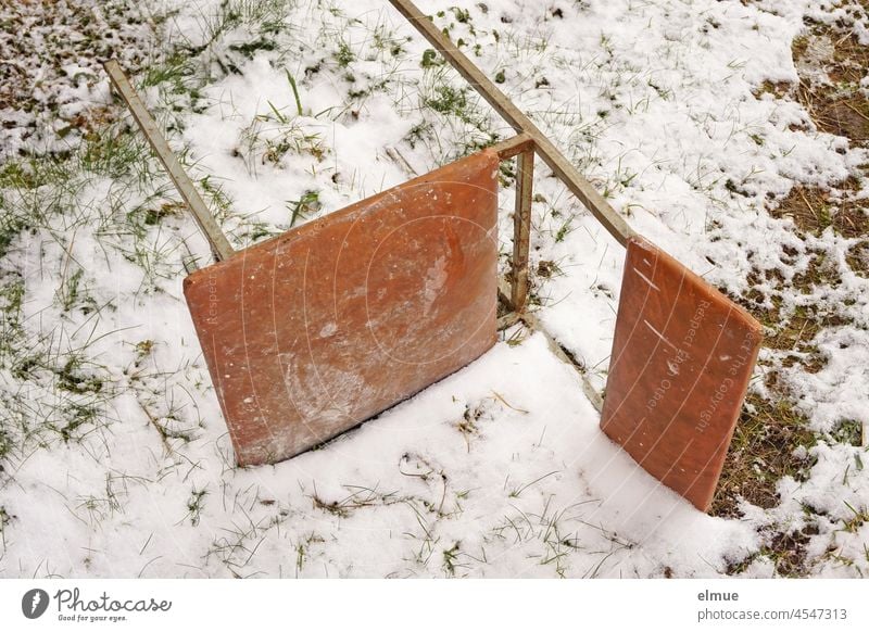 ein alter Küchenstuhl / Bürostuhl aus einem Metallgestell und braunem Kunststoffpolster liegt auf der schneebedeckten Wiese / Winter / Sitzmöbel Stuhl Schnee