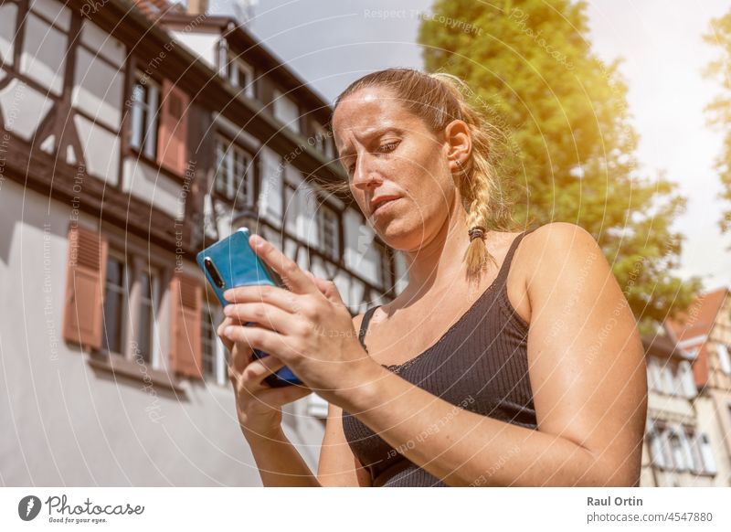 Weiblich mit Handy in der Stadt Hintergrund. Junge Frau mit einer App in Handy, Eingabe von Textnachricht auf traditionelle Häuser Hintergrund Person Telefon