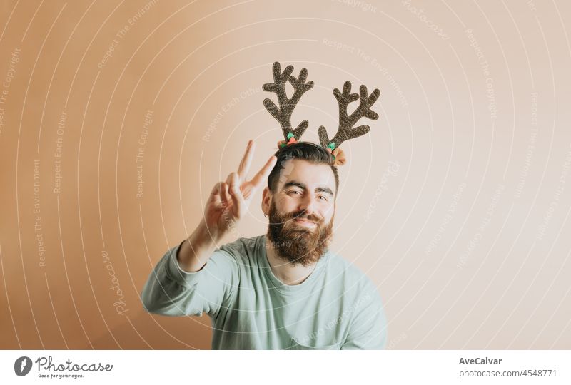 Junge Hipster Bart Mann in stilvollen Weihnachtskleidung, die Spaß mit einem bunten abnehmbaren Hintergrund. Neues Jahr Konzept. Spaß und spielerisches Konzept. Zeigen Kopie Raum, mit Smartphone,