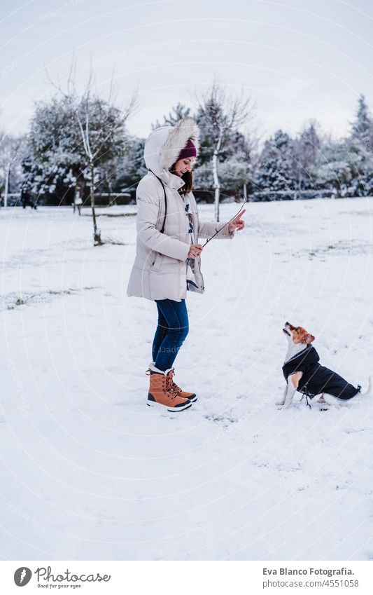 Frau in verschneiten Berg trägt modernen Mantel bei Sonnenuntergang. Spielen mit niedlichen Jack Russell Hund. Wintersaison. Spaß im Schnee jack russell