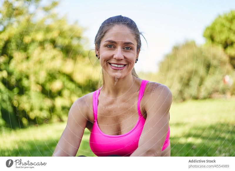 Fröhliche Sportlerin im Park sitzend Frau sportlich Sportkleidung Rasen Wellness Gesunder Lebensstil Training Fitness Baum Sportbekleidung passen Sommer heiter