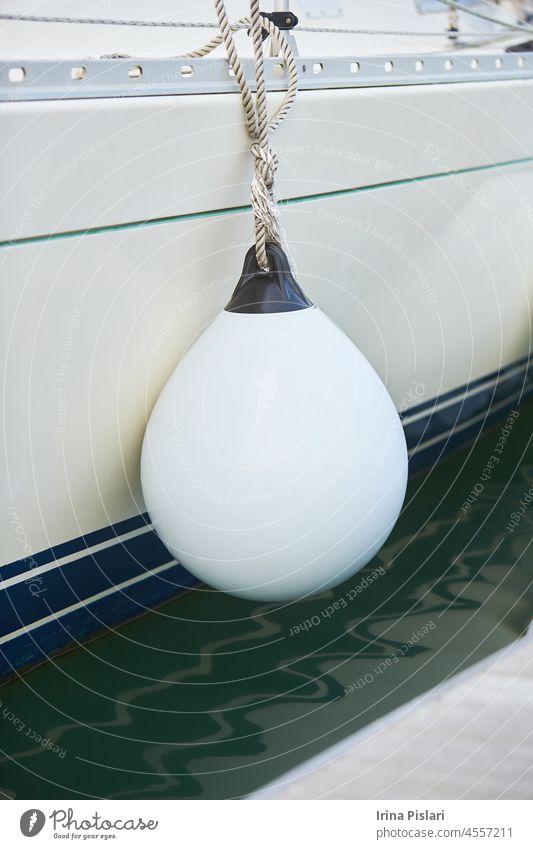 Weiße Fender, die zum Schutz zwischen einem Boot und dem Hafenbecken aufgehängt werden. Maritime Fender blau Holzplatte Bootfahren bouy Stoßstange Boje