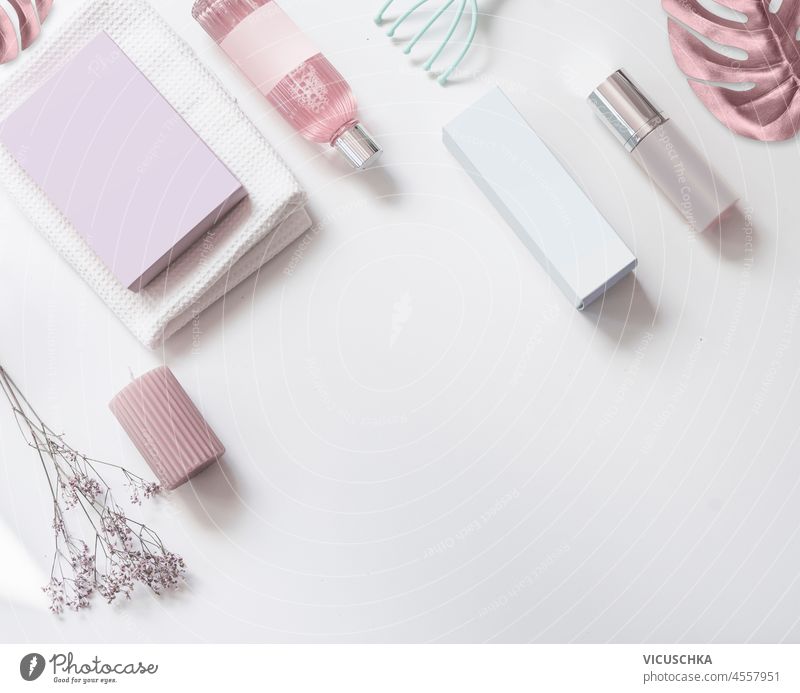 Schönheit Hintergrund mit verschiedenen kosmetischen Produkten, Spray-Flaschen, Boxen und rosa Blätter auf weißem Tisch. Rosa und weiße Kosmetik-Konzept mit leeren Etikett mock up. Draufsicht mit Kopierraum.