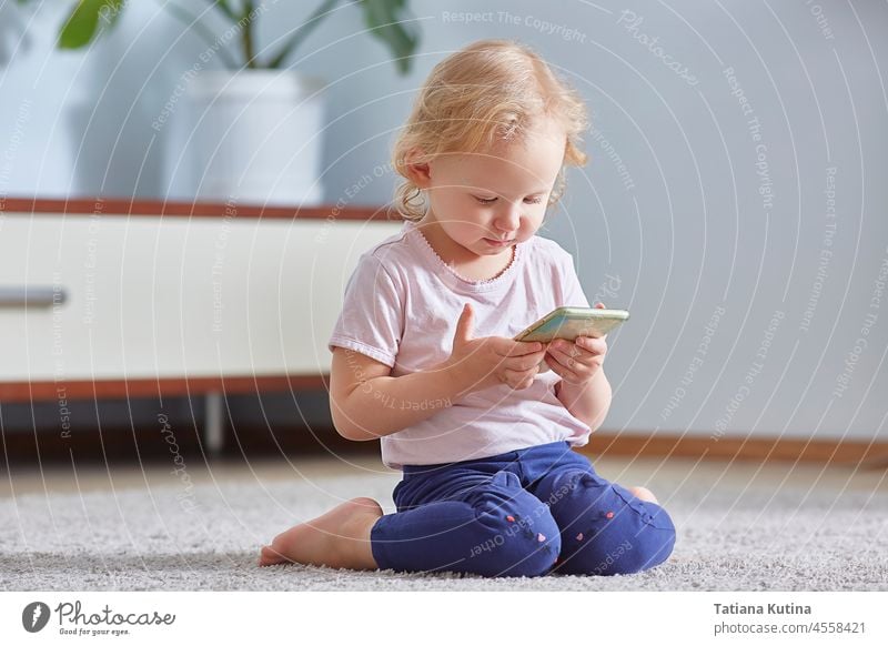 Kind Mädchen schauen Smartphone und sitzt auf dem grauen Teppich im Wohnzimmer. Kind Entwicklung Konzept. Telefon Technik & Technologie Mobile Bildschirm