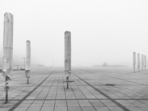 geschlossenen Sonnenschirme im Nebel auf einem großen Platz Nebelstimmung Nebelschleier Herbst Winter Winterpause Pause Stillstand Leere leerer Ort Ruhe Stille