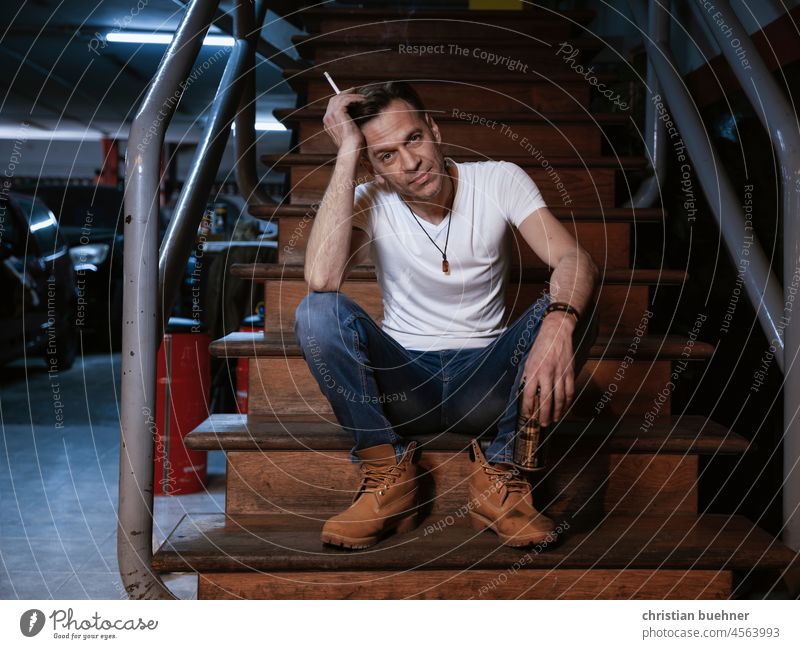 portrait eines 40 jaehrigen mannes in seiner autowerkstatt 40 jahre automechaniker garage treppe boots cool zigarette sexy autos easy symphatisch