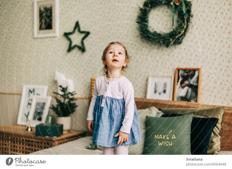 Ein glückliches Mädchen spielt am Weihnachtsmorgen auf dem Bett in einem für Weihnachten oder Neujahr dekorierten Zimmer. Kindheit, festlicher Morgen, Weihnachtsstimmung