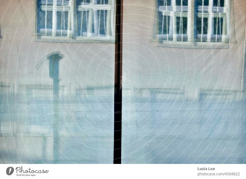 In den Fensterscheiben eines leerstehenden Straßencafés und dahinter hängenden Folien spiegelt sich die gegenüberliegende Fassade Glas Glasscheibe abhängt
