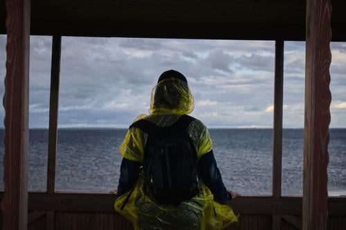 Frau schaut durch das Fenster auf das Wasser. Aktive Erholung außerhalb der Stadt. Die Tierwelt. Schlechtes Wetter Träume Nostalgie Verzweiflung Kontemplation