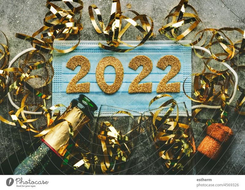 Silvesterfeier Konzept background.Medical Maske mit den Zahlen 2022 und Champagner-Flasche mit Gläsern.Covid-19 New Year Konzept auf grauem Hintergrund