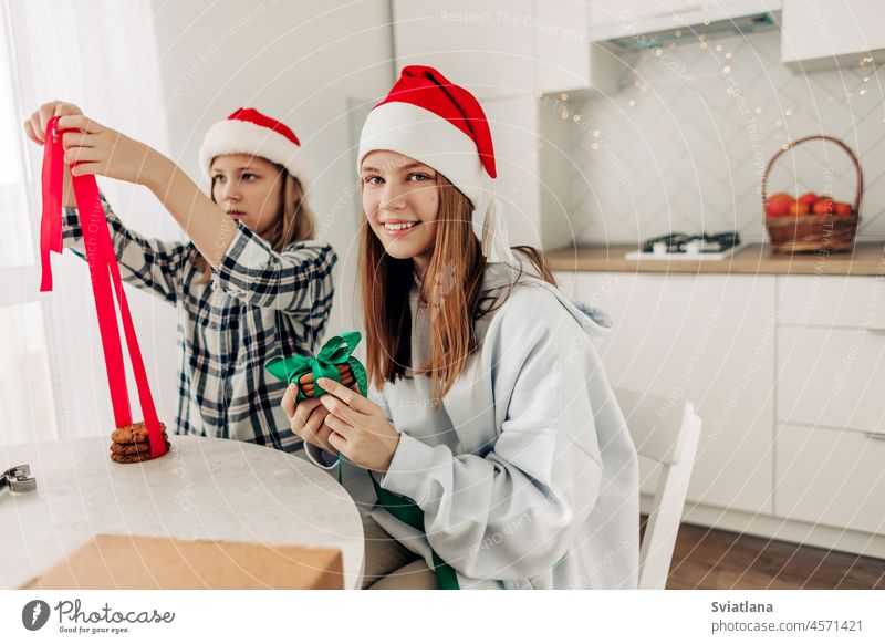 Zwei Mädchen verzieren Plätzchen mit leuchtend roten und grünen Bändern und bereiten süße Leckereien für Gäste an Weihnachten oder Silvester vor Geschenk neu