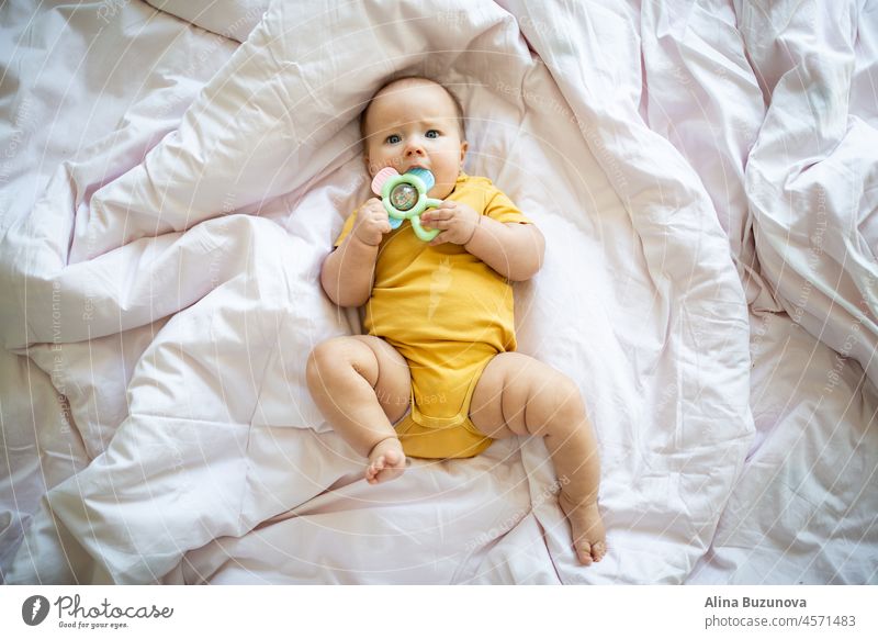 Kaukasische blonde Baby sieben Monate alt auf dem Bett zu Hause liegen. Kind trägt niedliche Kleidung gelbe Farbe neugeboren Säugling lichtvoll ultimativ grau