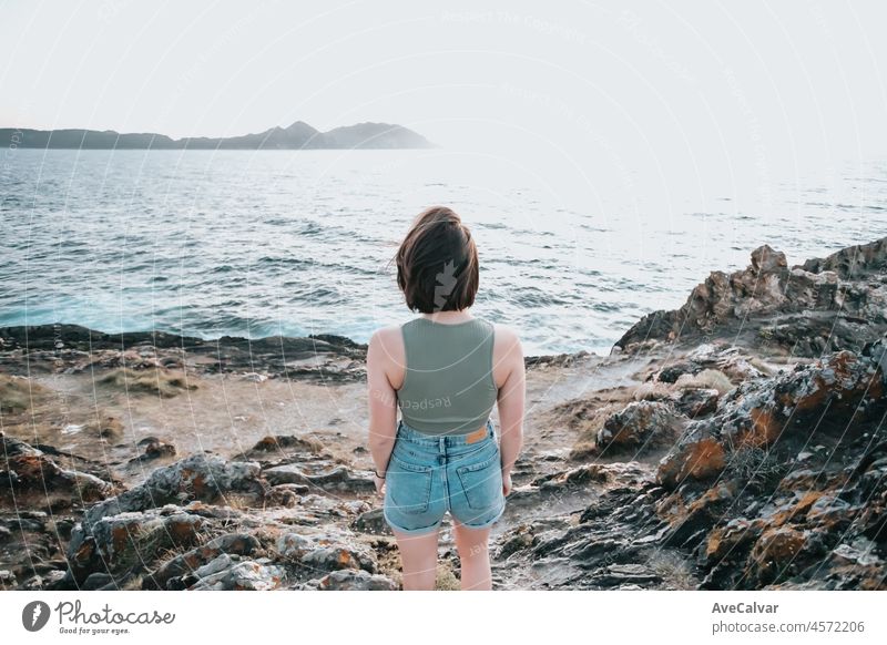 Eine junge Frau geht auf dem Pfad der Felsen am Ufer und blickt auf das abendliche Meer.Junge Hipster-Mädchen macht einige Wanderungen am Ufer, Reisen und Low-Budget-Reisekonzepte, Kopie Raum