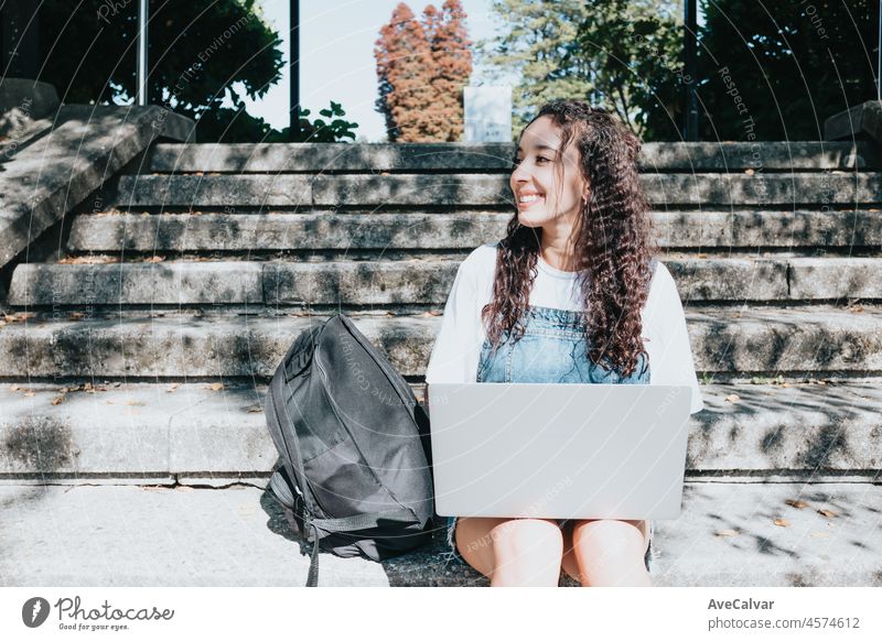 Fokussierte junge glückliche afroamerikanische Studentin, die auf einer Treppe an der Universität sitzt und einen Laptop benutzt, um über Universitätsarbeiten und Papier zu recherchieren. Bildung: Notizen machen, Online-Vorlesungen, Wissen gewinnen