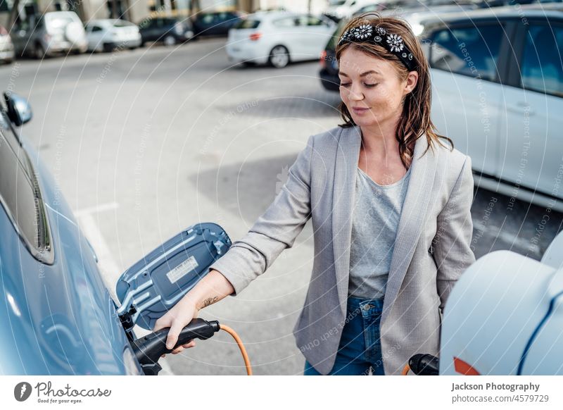 Eine elegante Frau, die ein Elektroauto in einer städtischen Umgebung auflädt PKW Gebühr Ladestation Kaukasier Erneuerbare Energie regenerativ Beteiligung