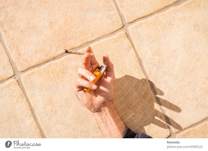 Eine Person liegt in der Sonne und hält einen Marihuana-Joint und ein Feuerzeug. Hintergrund einer Person, die sich in der Sonne entspannt und raucht. Gelenk