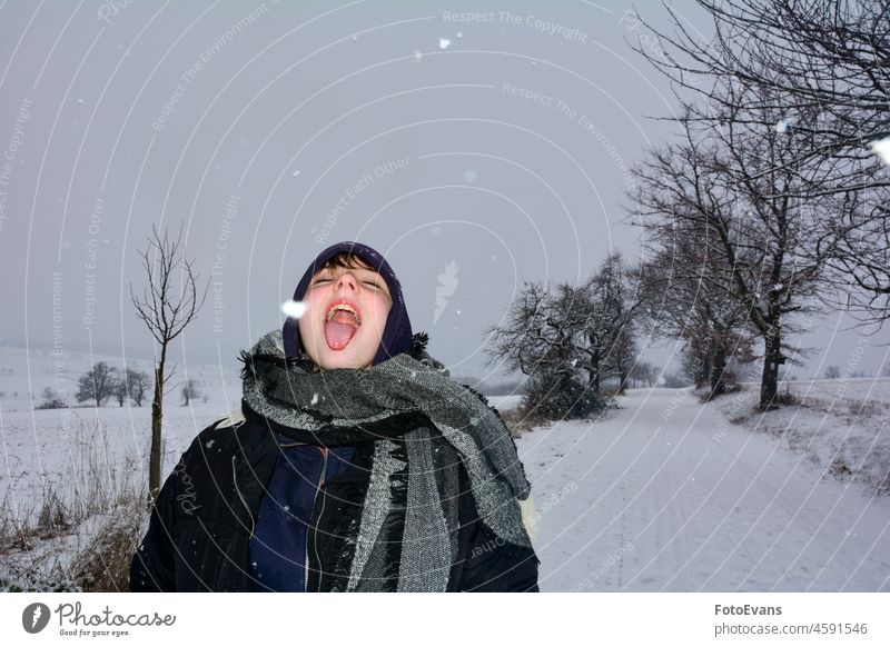 Mädchen in der Natur, fängt Schneeflocken mit ihrer Zunge Spaß Bekleidung Freude Schal Verschlussdeckel Mund Schuppen kalt Straße Bäume unbefestigter Weg Kind
