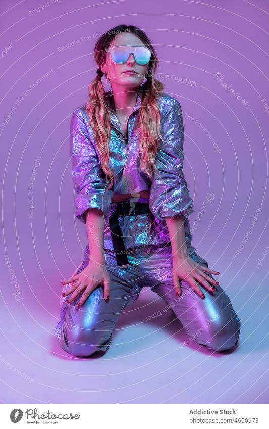 Trendige Frau mit Sonnenbrille steht auf den Knien in einem Neonstudio neonfarbig Model leuchten Vorschein trendy Atelier Bekleidung Persönlichkeit 80s Stil