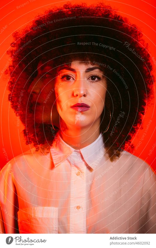 Ernste hispanische Dame in einem Studio mit roten Neonröhren stehend Frau ernst Model Porträt Vorschein Stil selbstbewusst selbstsicher neonfarbig traumhaft