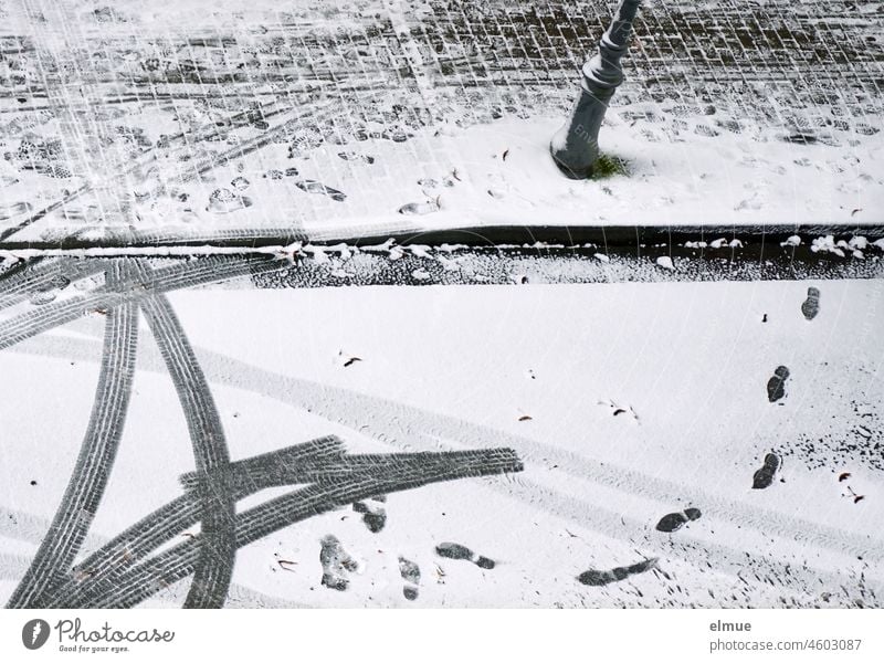Fußspuren und Autoreifenspuren auf der schneebedeckten Straße und dem gepflasterten Fußweg mit Straßenlaterne aus der Vogelperspektive / wegfahren / Winter