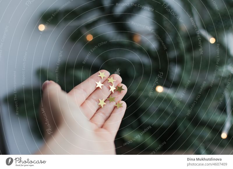 Hand hält glitzernde goldene Sterne mit Weihnachtsbaum als Hintergrund. Minimalistisches Weihnachtsfoto. Beteiligung magisch Zauberei u. Magie Vorstellungskraft