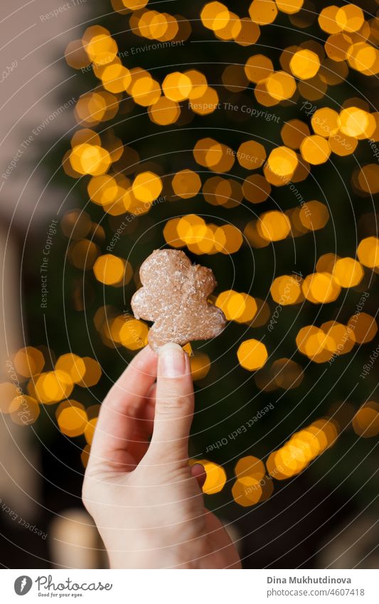 Hand hält eine hausgemachte Lebkuchenmann Keks mit Weihnachtsbaum Lichter Bokeh als Hintergrund altehrwürdig Glück neu Jahr Weihnachten festlich Neujahr