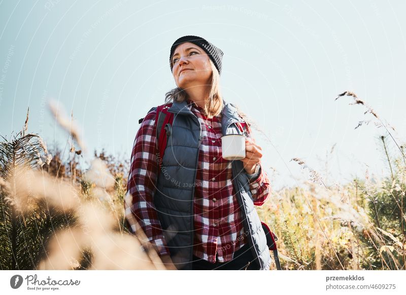 Frau macht Pause und entspannt sich mit einer Tasse Kaffee während eines Sommerausflugs. Frau steht auf dem Weg und schaut weg. Frau mit Rucksack Wandern durch hohes Gras entlang Weg in den Bergen