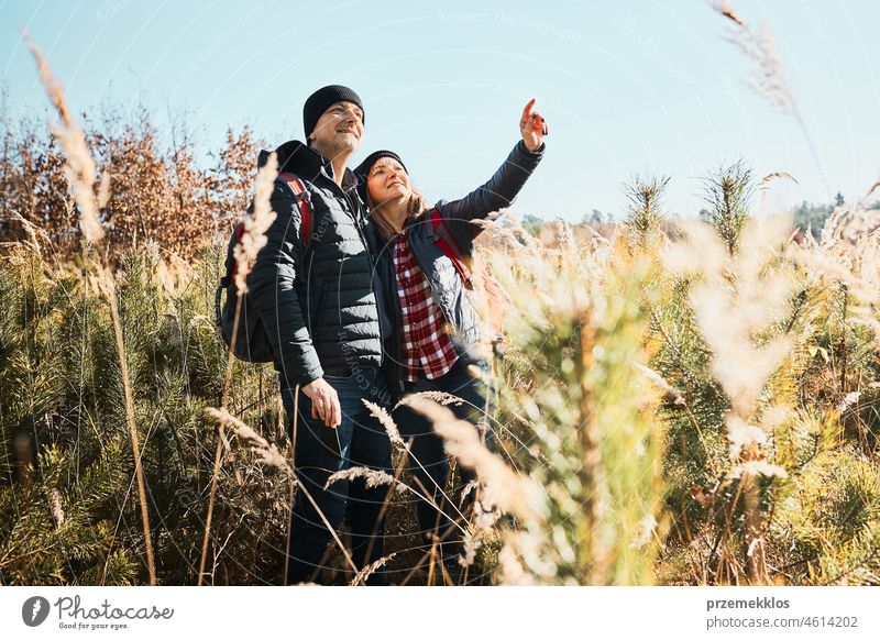 Ehepaar erkundet die Natur auf einer Urlaubsreise. Wanderer mit Rucksäcken auf dem Weg in die Berge. Menschen zu Fuß durch hohes Gras entlang Weg in der Wiese an einem sonnigen Tag