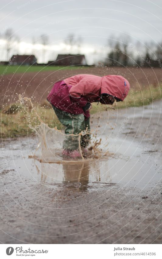 Mädchen hüpft in Riesenpfütze Regenwetter ungemütlich Kindheit Kindergarten Spielen toben draußen draußen sein glücklich frech platsch nass Wasser spritzig