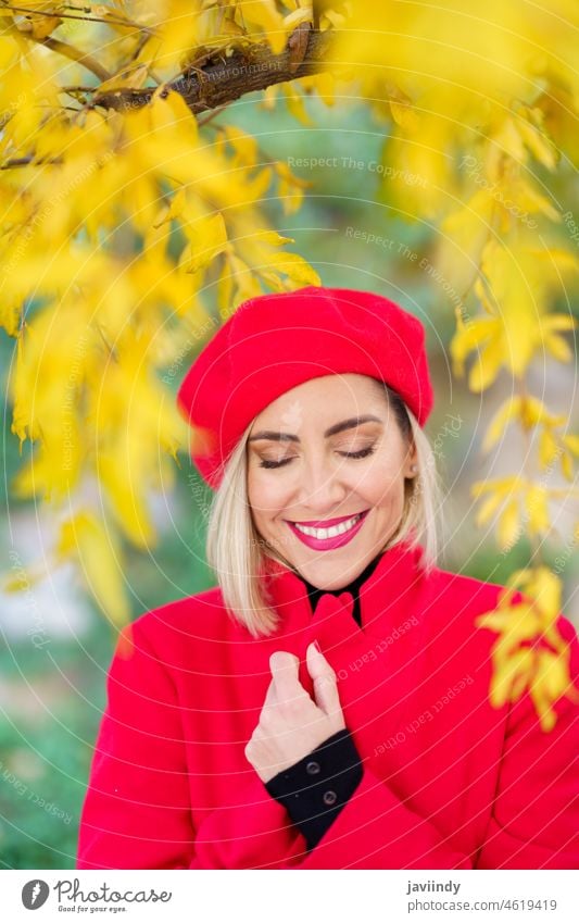 Glückliche Frau mittleren Alters, die mit geschlossenen Augen zwischen Herbstblättern lächelt. Winter rot Baskenmütze Mantel urban Mitte Lebensalter fallen Mode