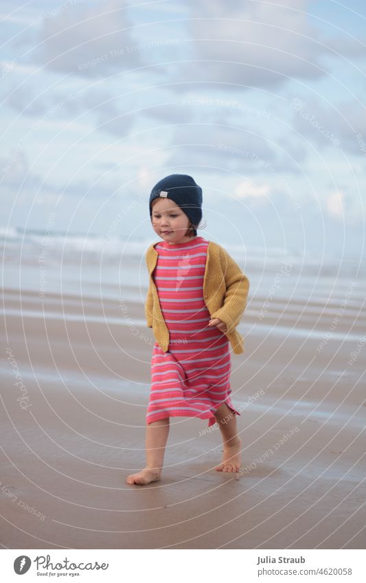 kleines Mädchen mit Mütze rennt am Strand barfuss Meer idyllisch traumhaft schön Wolken Himmel Wellen barfüßig Barfuß laufen rennen Bewegung bewegen Kleid