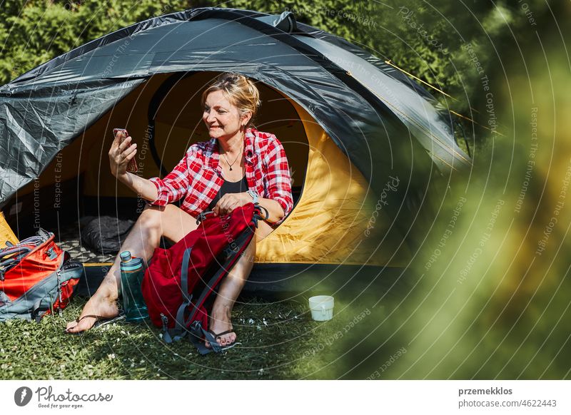 Eine Frau führt einen Videoanruf mit Freunden über ihr Smartphone, während sie im Zelt beim Camping sitzt. Frau entspannt im Zelt während des Sommerurlaubs
