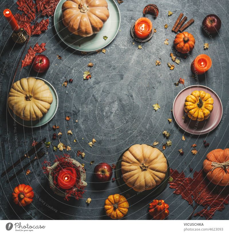 Verschiedene Kürbisse auf Tellern mit orangefarbenen Kerzen, Besteck und Herbstblättern auf dunklem, rustikalem Hintergrund. Rahmen verschiedene Platten Blätter