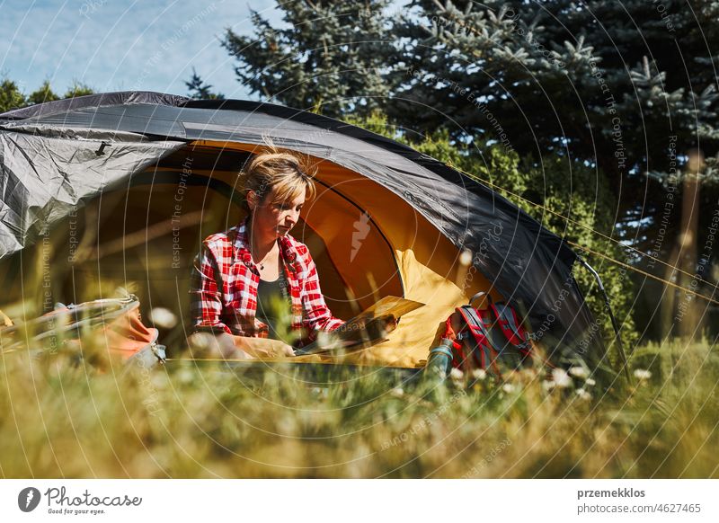 Frau plant nächste Reise, während sie mit Karte im Zelt sitzt. Frau entspannt im Zelt beim Camping im Sommerurlaub Urlaub Ausflug Abenteuer Campingplatz reisend