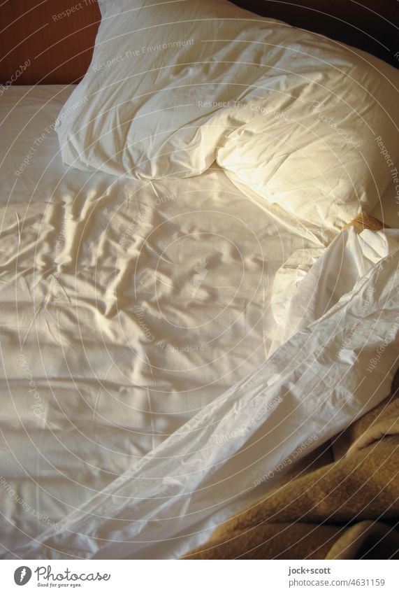 zerwühltes Bettlaken am Morgen mit den ersten Sonnenstrahlen Hotelbett Bettwäsche Bettdecke Decke Menschenleer Kissen weiß gemütlich Kopfkissen benutzt Falten