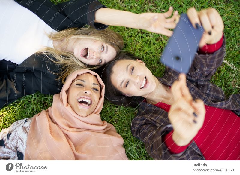 Fröhlich diverse Freundinnen lachen und nehmen Selfie auf Rasen im Park liegen Frauen Lügen Smartphone Zusammensein bester Freund Zeit verbringen Freundschaft