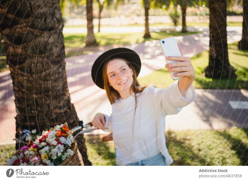 Frau nimmt ein Selfie gegen ein Fahrrad mit Blumen Smartphone Park Radfahrer Lächeln Handfläche tropisch Sommer Stil Selbstportrait positiv heiter Telefon
