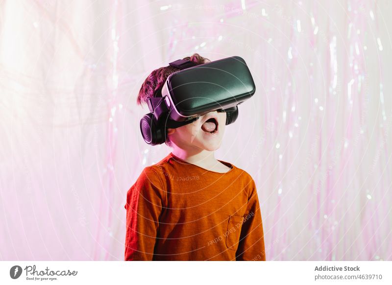 Staunender Junge mit VR-Brille im Studio Kind Schock erstaunt Schutzbrille Virtuelle Realität Cyberspace Headset unterhalten neonfarbig Licht Erstaunen virtuell