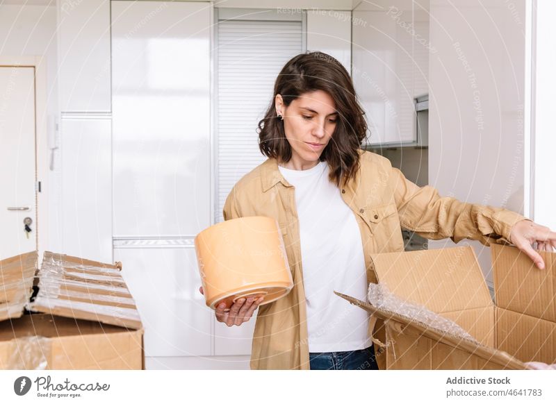 Frau beim Auspacken eines Kartons auf dem Boden auspacken Kasten Stock einziehen Appartement Küche Zugehörigkeit Tisch offen Paket neu Schachtel verweilen Topf