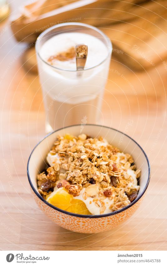 vorne im Bild ist eine Müslischüssel mit Obst, Granola und Quark dahinter steht ein Latte Macchiato im Glas Kaffee Frühstück Essen Milch gesund werden