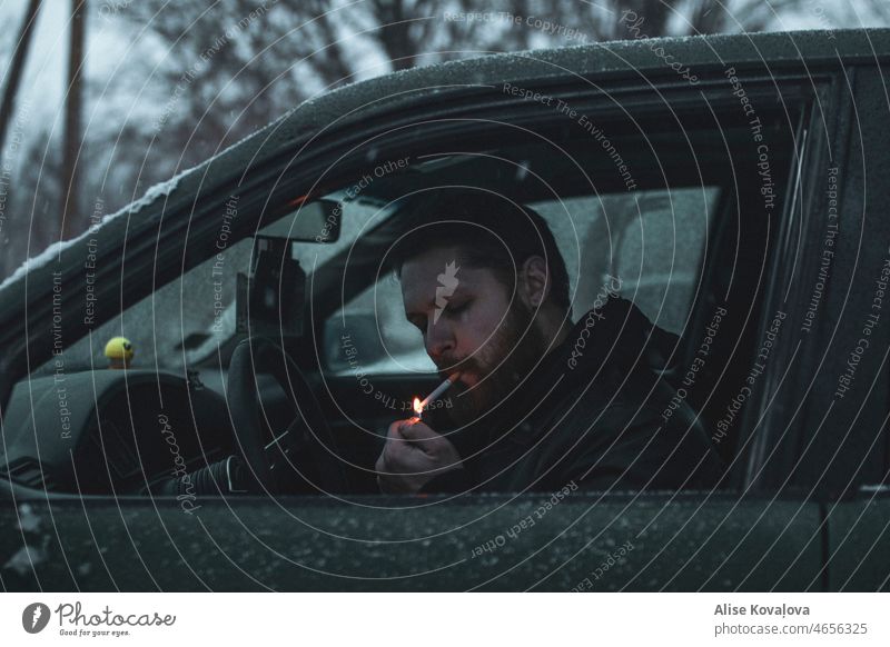 Mann zündet sich im Auto eine Zigarette an Porträt Anzünden einer Zigarette In einem Auto Nikotin Rauchen ungesund Winter Schnee Filterzigarette Beleuchtung