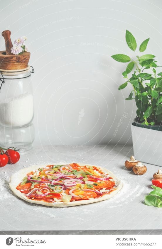 Selbstgemachte Pizza am weißen Küchentisch mit Glasgefäß mit Mehl, Basilikum und Zutaten selbstgemacht Tisch Bestandteil Essen zubereiten traditionell