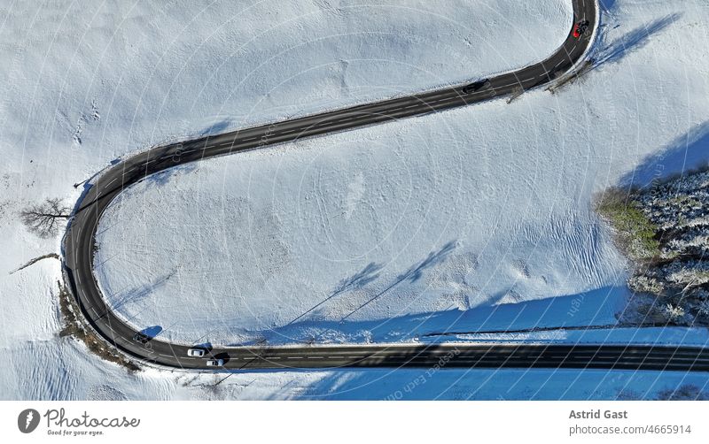 Luftaufnahme mit einer Drohne von einer verschneiten Landschaft mit einer kurvigen Straße mit Autos luftaufnahme drohnenfoto Winter Schafe autos Kurve kehre